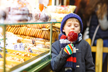 Happy child eating on apple covered with red sugar on Christmas market