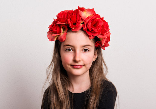 A close-up of small girl with flower headband sitting in a studio.