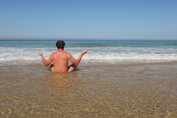 naked man on water beach make yoga in back view in summer day