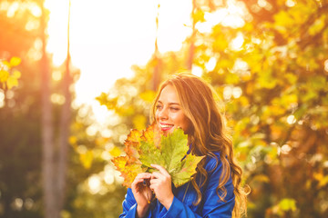 Cute smiley woman holding autumn leafs in the nature.