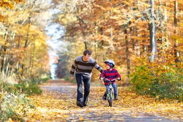 Little kid boy and his father in autumn park with a bicycle. Dad teaching his son biking