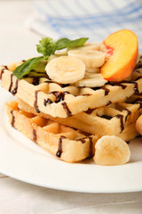 Belgian waffle with peach and banana in plate on wooden table.