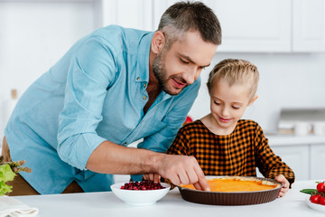 happy father and adorable little daughter decorating pumpkin pie for thanksgiving day