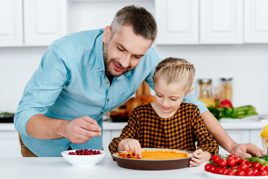 father and adorable little daughter decorating pumpkin pie for thanksgiving day