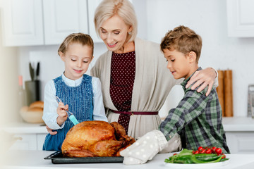 adorable siblings preparing thanksgiving turkey with grandmother at kitchen