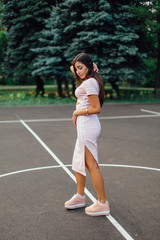 Charming brunette female dressed in a pink dress posing on the basketball court.