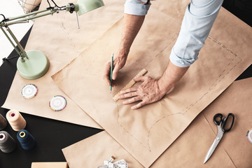 Mature tailor working with sewing pattern in atelier