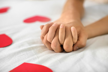 Young couple with red hearts holding hands while lying on bed at home
