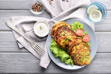 Plate with tasty zucchini pancakes on wooden table