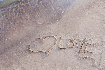 Heart and word LOVE written on beach sand