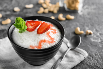 Bowl with delicious rice pudding and strawberry on dark background