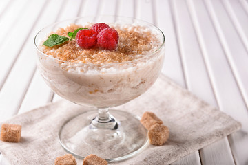 Bowl with delicious rice pudding and raspberry on white table