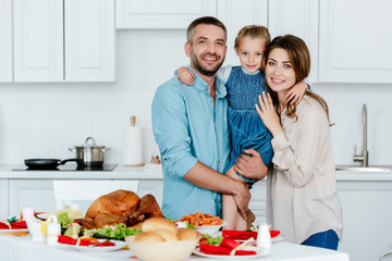 happy family with adorable little daughter standing near served table for thanksgiving dinner