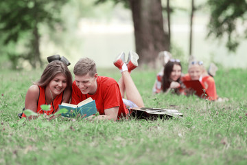 smiling couple of students reading a book lying on the grass