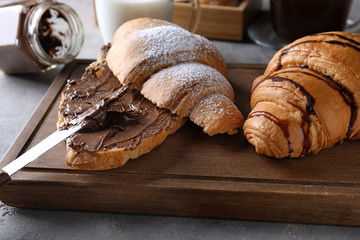 Tasty croissants with chocolate paste on wooden board