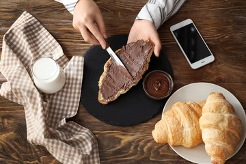 Woman spreading croissant with chocolate paste on slate plate