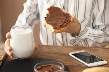 Woman eating tasty croissant with chocolate and milk at table