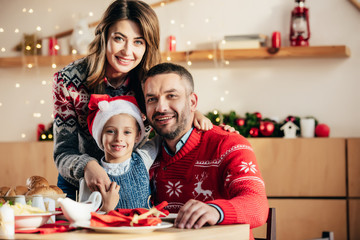 portrait of happy family with daughter in christmas hat sitting at table with holiday dinner