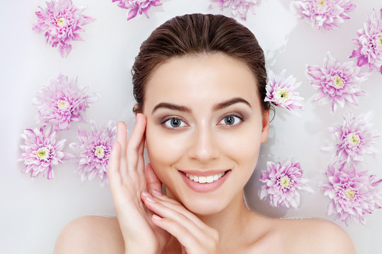 Portrait of young sexy beauty female woman smiling with clean pure skin taking spa relaxing in bath with flowers and white soap shampoo water. Skin beauty health care concept. Body part and nature
