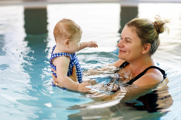 Happy mother swimming with cute adorable baby girl daughter in swimming pool spending spa vacations