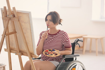Young female artist in wheelchair painting picture at home