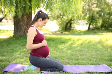 Young pregnant woman sitting on yoga mat outdoors