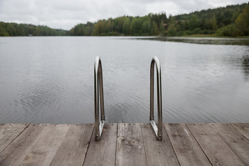 Metal handrail for descent into the lake,  iron ladder for swimmers. Wooden pier on the lake,...