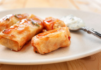 Plate with stuffed cabbage leaves in tomato sauce on wooden table, closeup