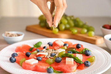 Woman adding sunflower seeds to sweet salad with watermelon and feta on plate, closeup