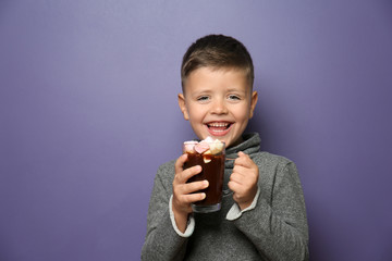 Cute little boy with glass cup of hot chocolate on color background