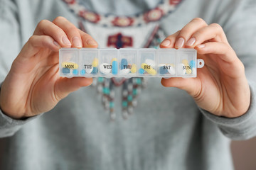 Woman holding plastic container with different pills, closeup