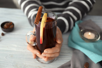 Woman holding glass cup of delicious mulled wine on wooden table, closeup