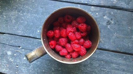 Ripe raspberries in a tin mug on a vintage table