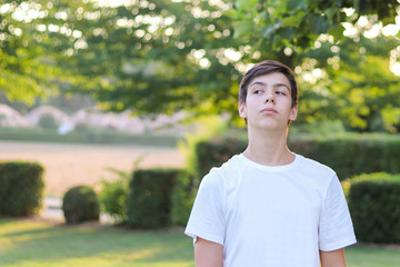 Teenager boy in white shirt looking arrogantly and  offended at someone, outside at summer park....