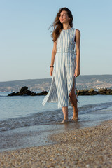 Fototapeta na wymiar beautiful stylish woman in a barefoot dress walking in the surf band