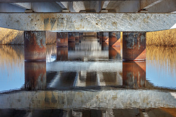 Fototapeta na wymiar The lower part of the concrete bridge with steel columns and water surface