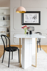 Black chair at table with flowers in white dining room interior with poster and lamp. Real photo