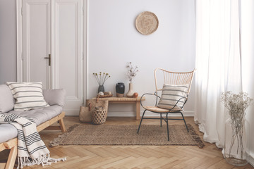 Armchair on rug next to bench with plants in white loft interior with wooden sofa. Real photo