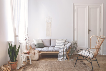 Wooden sofa with cushions in white living room interior with plant and armchair. Real photo