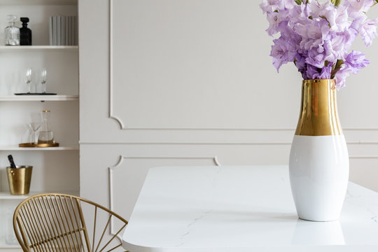 Violet flowers on white table in simple dining room interior with wall with molding. Real photo