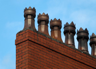 A row of old fashioned traditional clay chimney pots on a red brick support against a blue sky from when houses where built coal burning heating