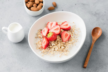 Fototapeta na wymiar Oatmeal porridge with strawberries and almond milk. Vegetarian or vegan breakfast. Concrete background