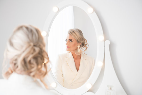 Young woman putting on earrings in front of mirror