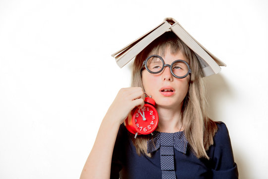 Portrait of a nerd girl in glasses with books and alarm clock on white background