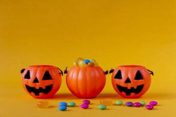 Halloween Jack o Lantern bucket filled with candies on yellow background