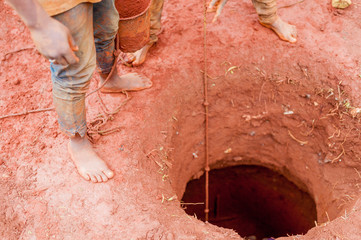 detail of bare feet african boys building water well in red african soil manually