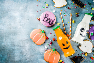 Kids treats for Halloween, funny homemade glazed cookies, various candies milk and juice in monster bottle, blue concrete background copy space top view