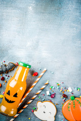 Kids treats for Halloween, funny homemade glazed cookies, various candies milk and juice in monster bottle, blue concrete background copy space top view