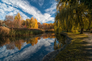 Beautiful autumn park with colorful trees and pacturesque sky reflected in the water