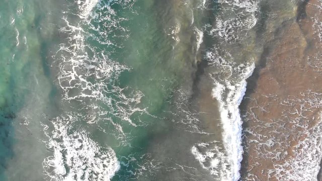 Waves create texture from white sea foam. Overhead drone footage perspective. Aerial footage of waves. 